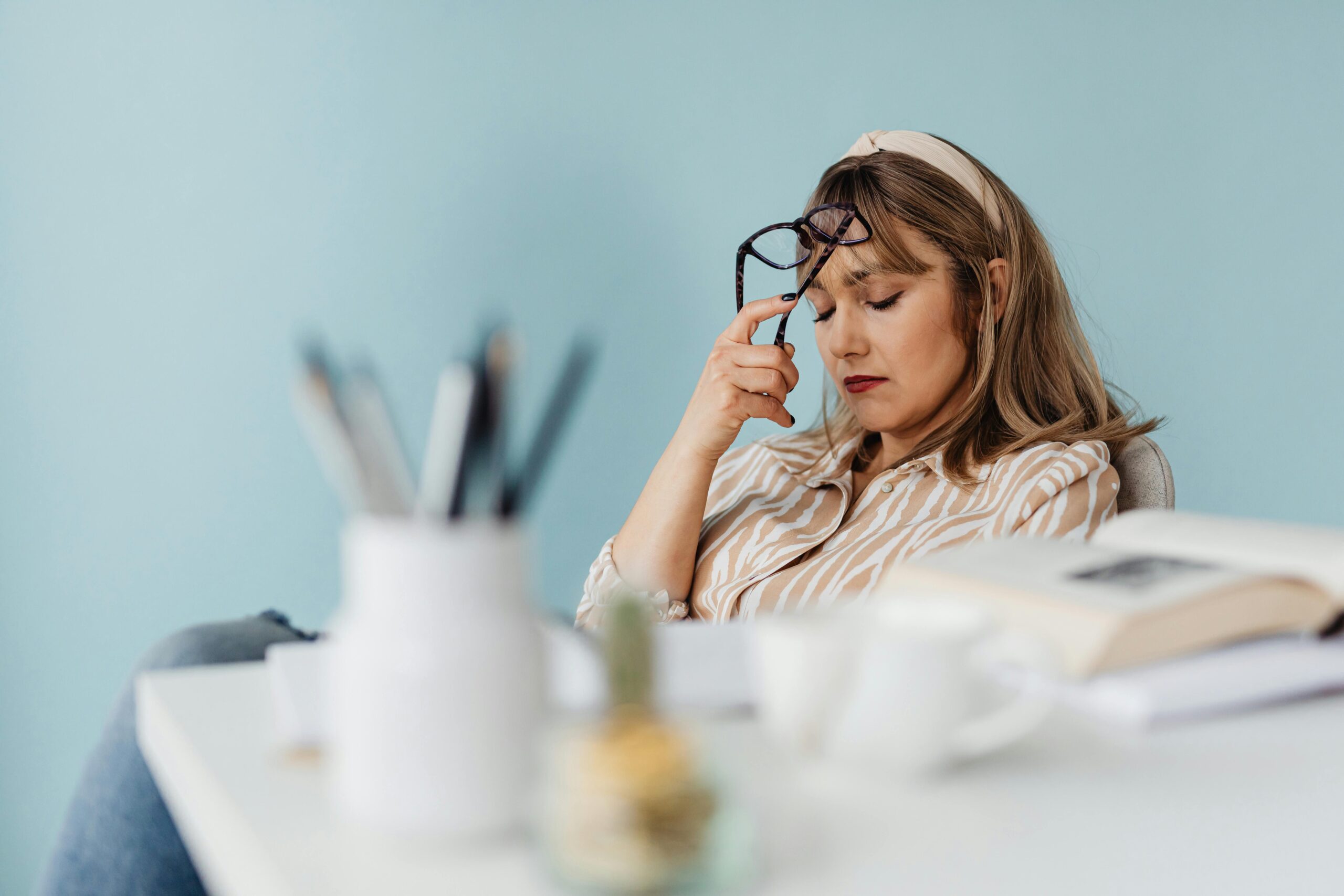 Stressed woman sitting at her desk in an office, resting her forehead in her hand, symbolizing mental health awareness.