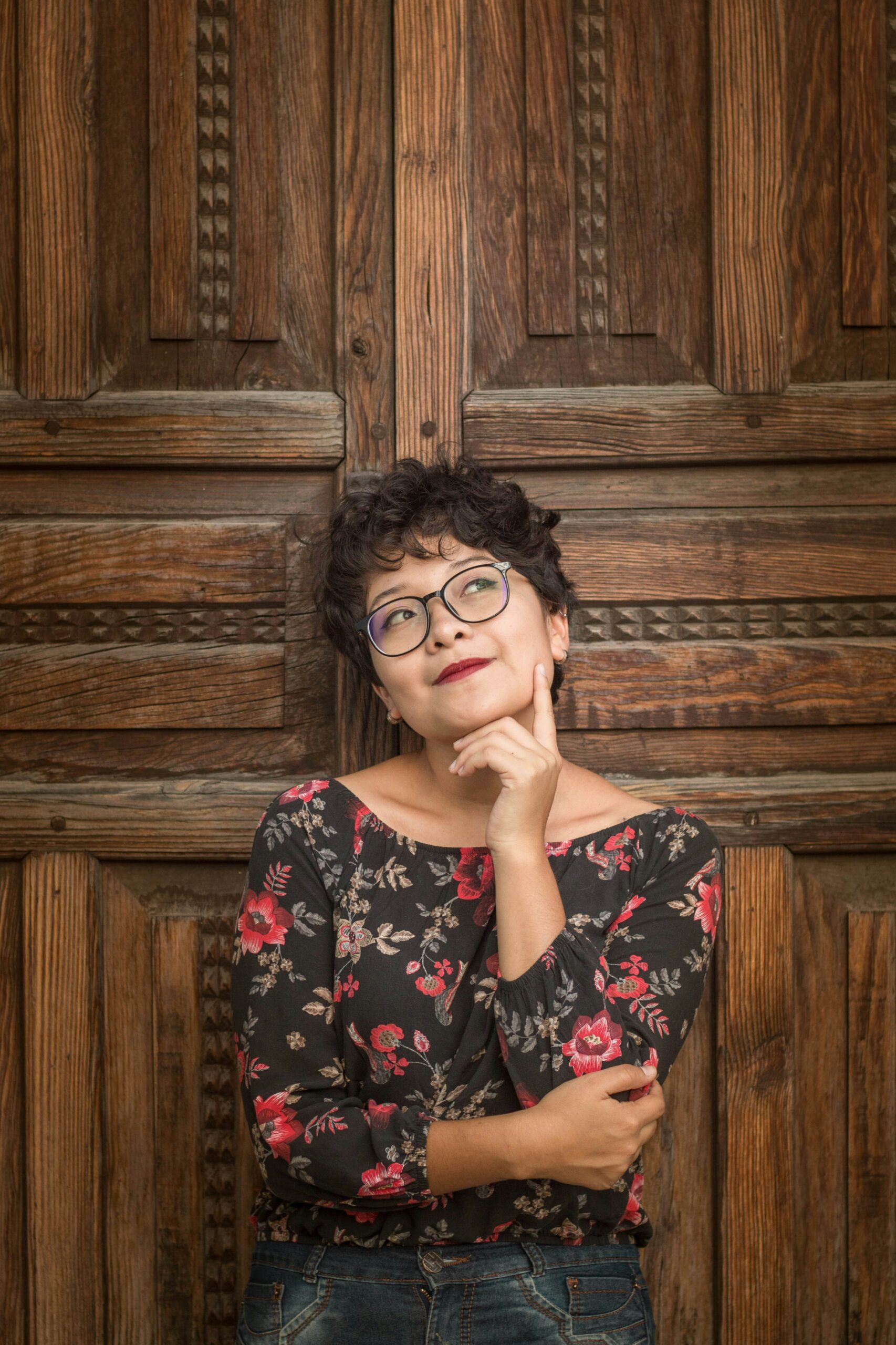 Photo of a woman standing near a wooden door, deep in thought. She has a thoughtful expression, illustrating the process of brainstorming and generating ideas.