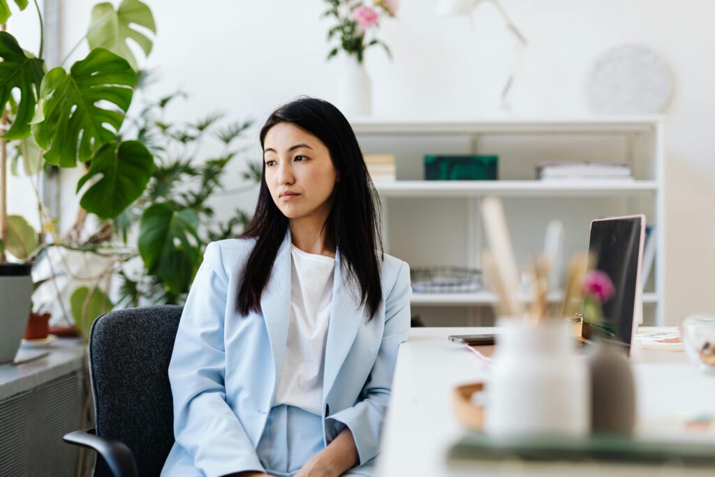 A woman seated at a desk in a bright office, looking away thoughtfully during a moment of career reflection and transition.