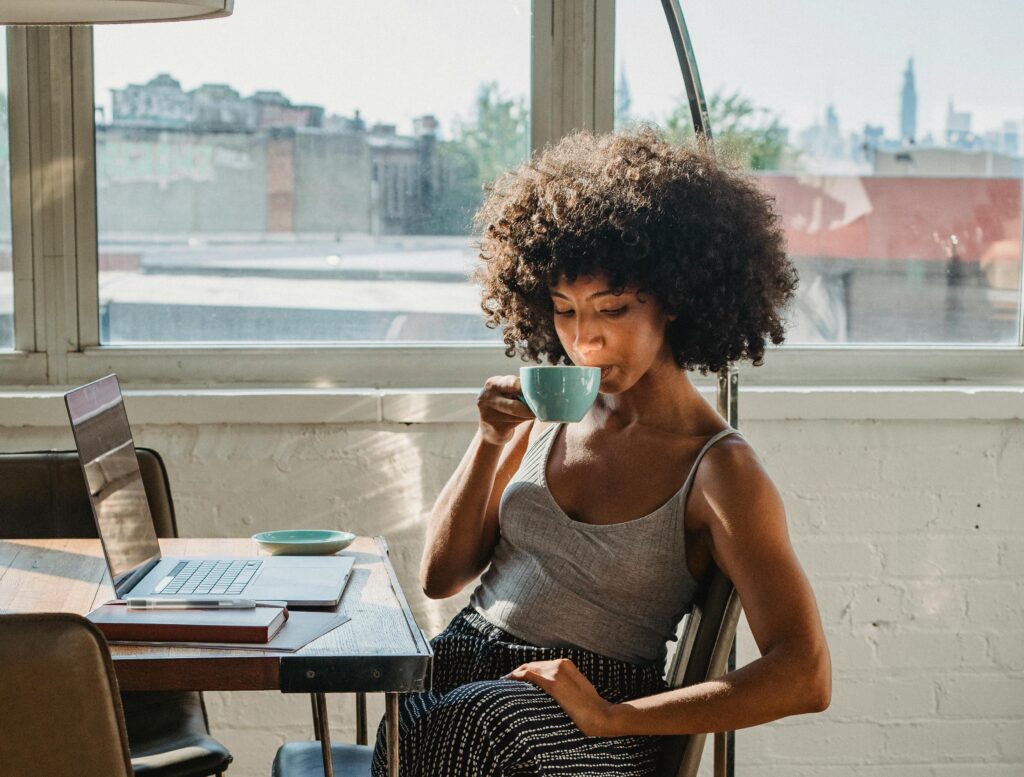 Freelance woman sitting at her laptop leisurely enjoying a cup of coffee.