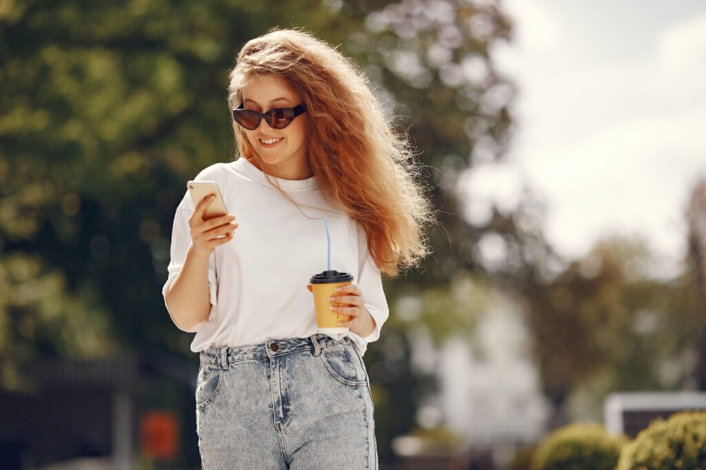 A woman walking happily with coffee and phone.