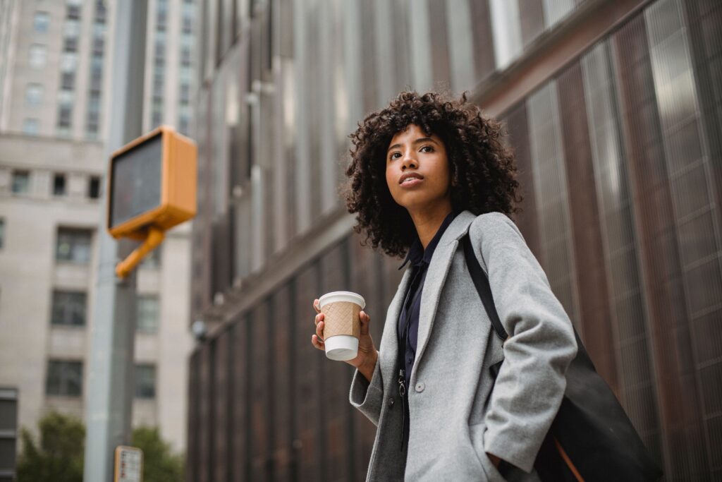 A fashionable woman holding a coffee cup in an urban setting, looking confident and stylish.
