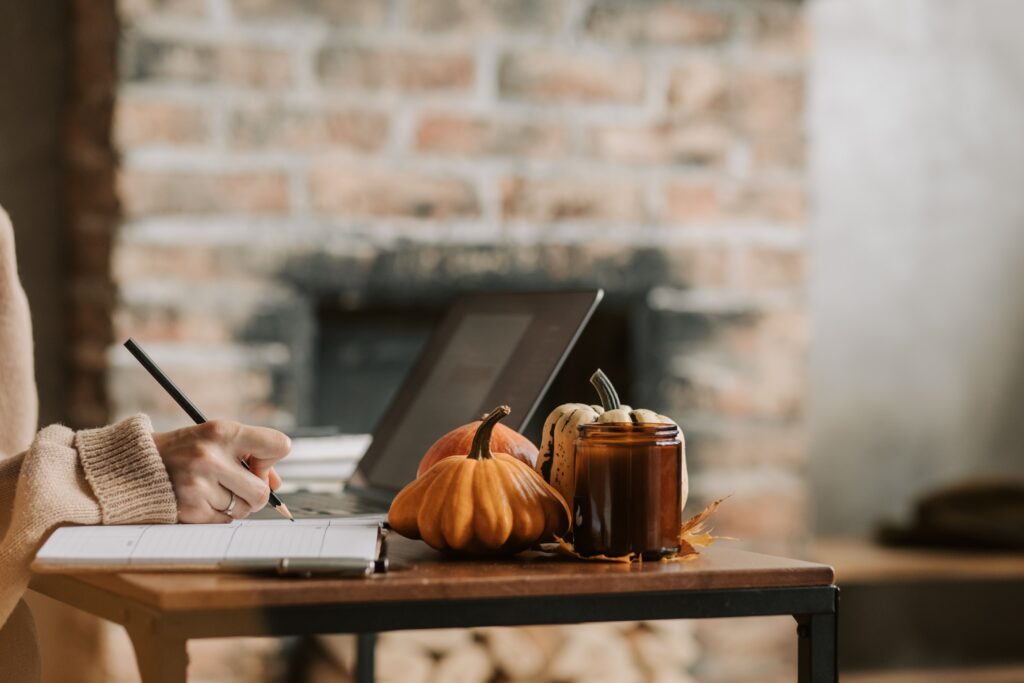 A cozy indoor workspace featuring writing in a notebook beside pumpkins and a candle.
