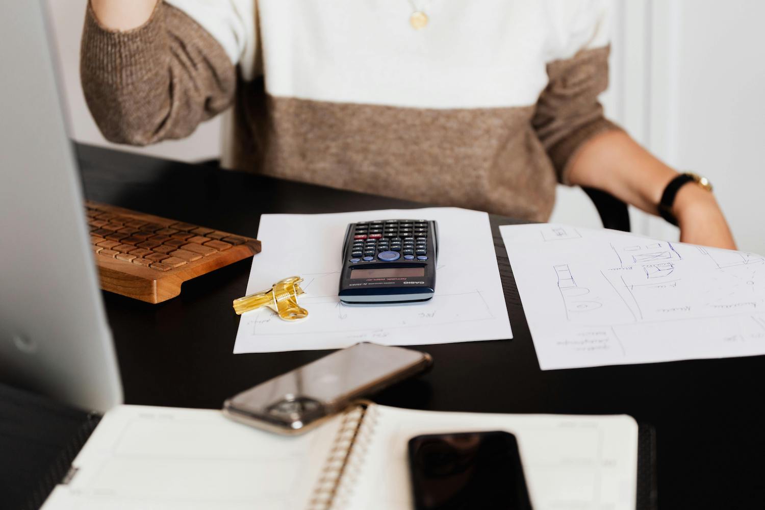 A woman working at her desk with financial documents, a calculator, keys, and a smartphone, emphasizing financial planning for small businesses.